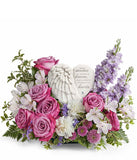 Sympathy flower arrangement with lavender roses, white alstroemeria, white carnations, lavender stock, lavender button spray chrysanthemums, and greenery, surrounding a  heart-shaped keepsake with angel wings and an inscription about loved ones in heaven.
